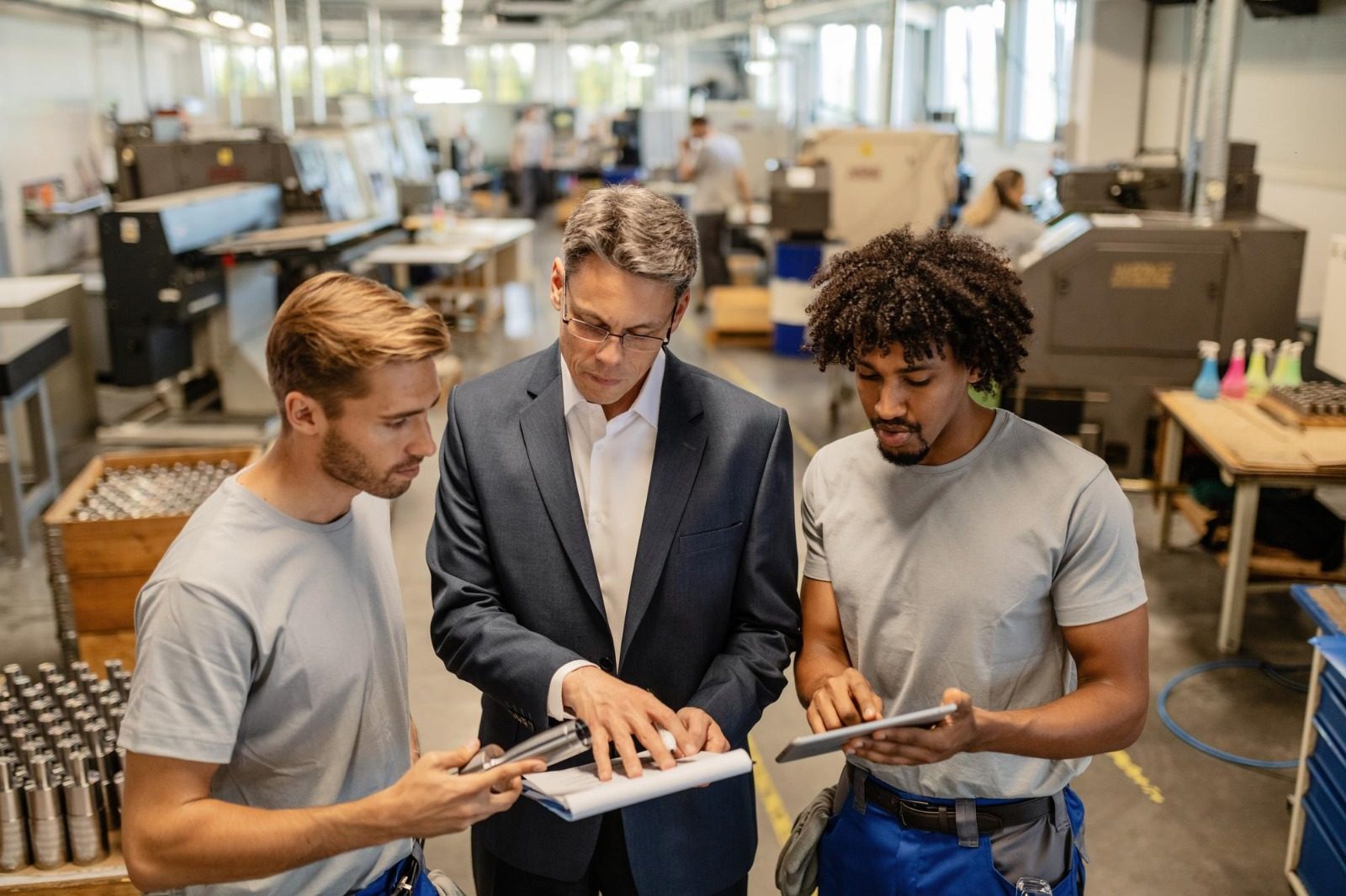 An industry expert mentoring two young technical trainees on a factory floor